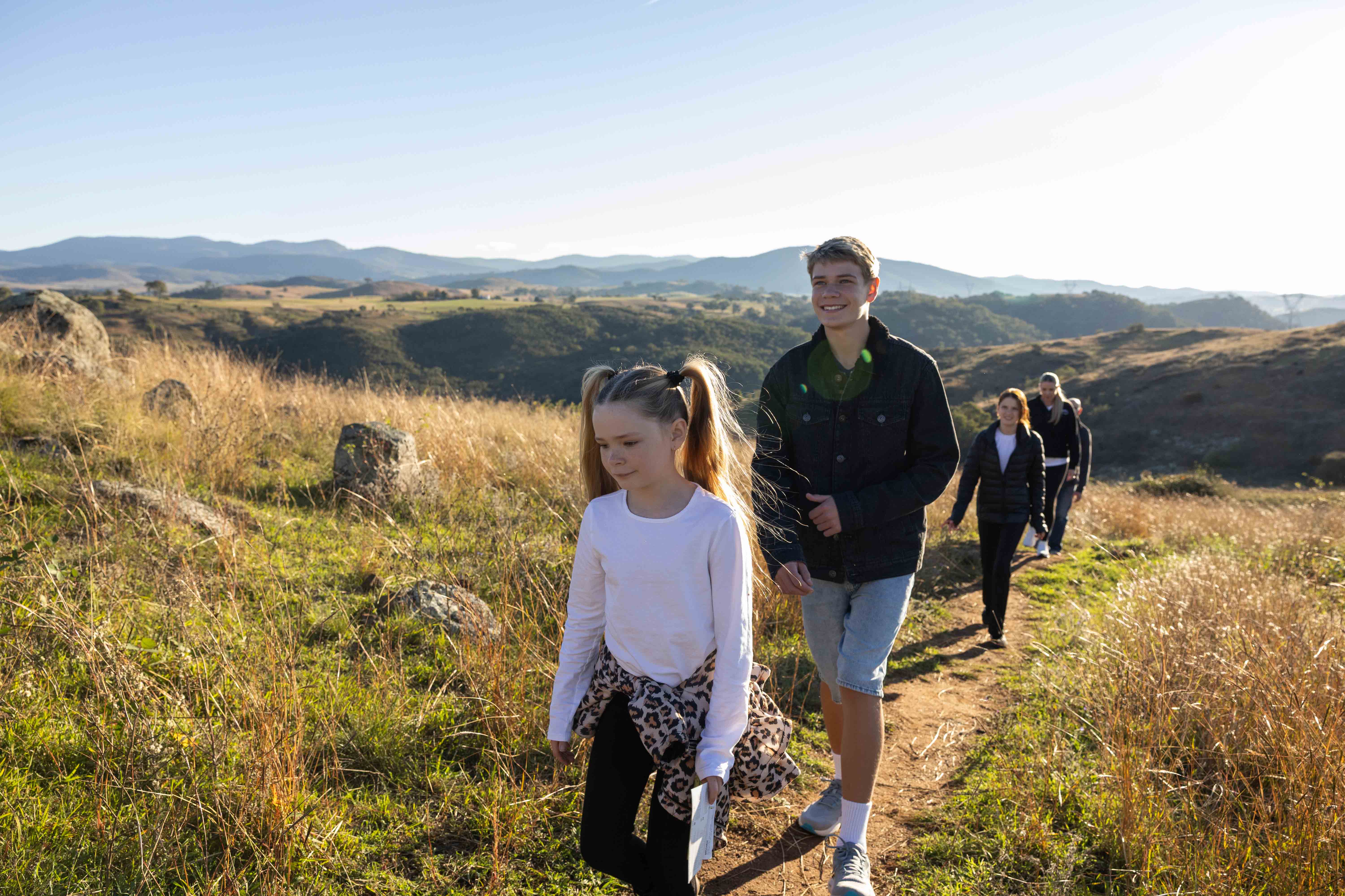 A family hiking together along a narrow path on a grassy hillside.