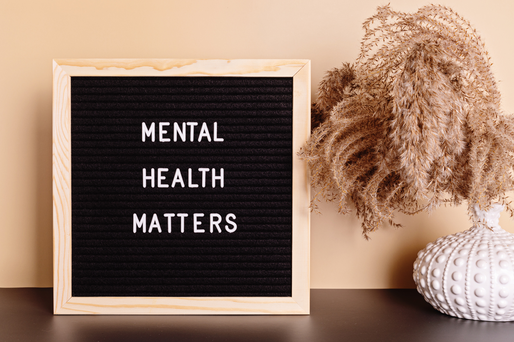 Sign reading “Mental Health Matters” beside a small vase of dried plants on a table.