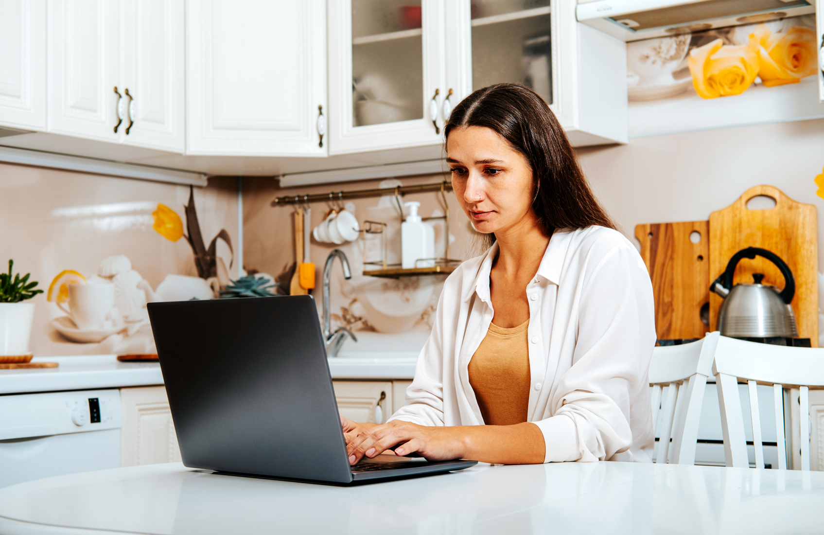 A person sitting at a table in a kitchen using a laptop.