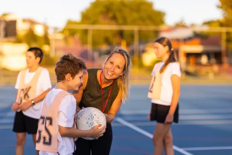 A child holding a ball on a netball court, near umpire and with other children nearby.