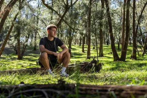 A person sitting on a fallen log in a forest area.