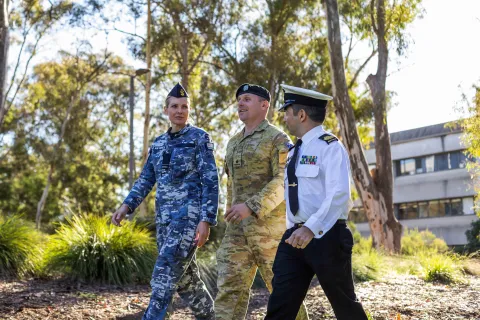 Three people in different Australian Defence Force uniforms walking side by side in a park.