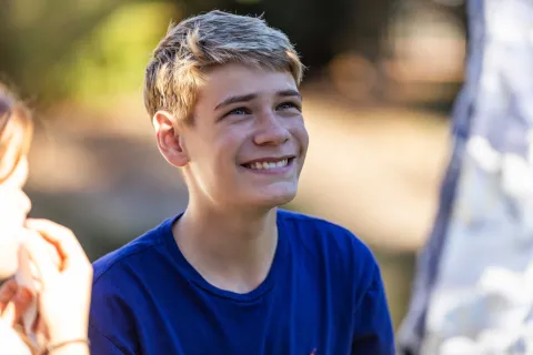 Close-up of teenage boy sitting outdoors, looking up at someone standing nearby.