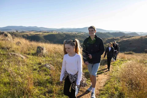 A family hiking together along a narrow path on a grassy hillside.