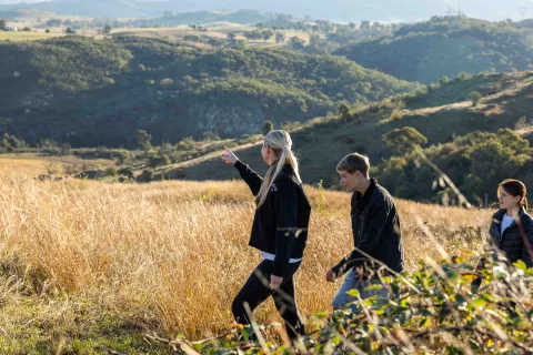 An adult and two teengage children walking together through a grassy hillside landscape, with the adult pointing into the distance.