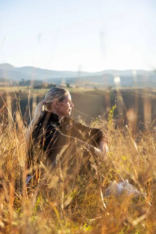 A person sitting in tall grass on a hillside, looking out over the landscape.