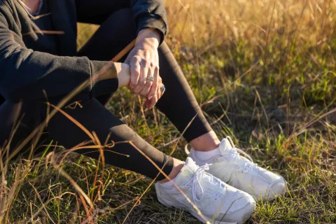 Close-up of a person clasping their hands while sitting in tall grass on a hillside.
