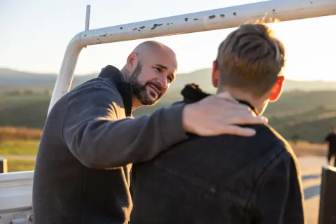 An adult resting a hand on a teenager's shoulder while talking at the back of a vehicle.