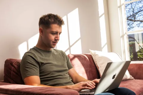 A person sitting on a couch at home using a laptop.