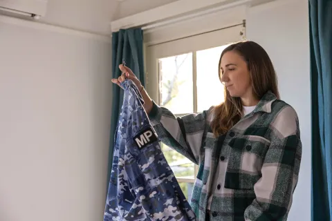 A person holding and looking at their Australian Defence Force uniform on a hanger by a window.
