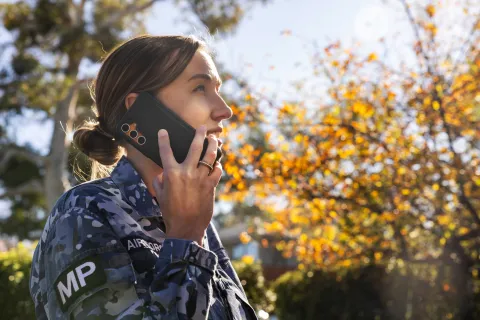 Close-up of a person in an Australian Defence Force uniform talking on a mobile phone outdoors.