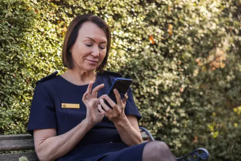 A person in Australian Defence Force uniform sitting on a bench in a garden setting, using a mobile phone.