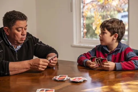 An adult and child sitting at a table playing a card game together.