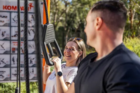 Two people using outdoor exercise equipment in a park setting.