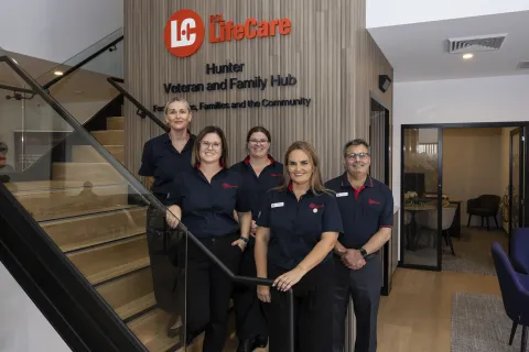 Five staff members in uniform standing together near a staircase inside the Hunter Veteran and Family Hub, with signage on the wall behind them.