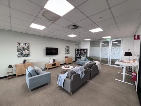 Seating area inside the Northern Adelaide Veteran and Family Hub with couches, a small table, television and shelves in a light-filled room.