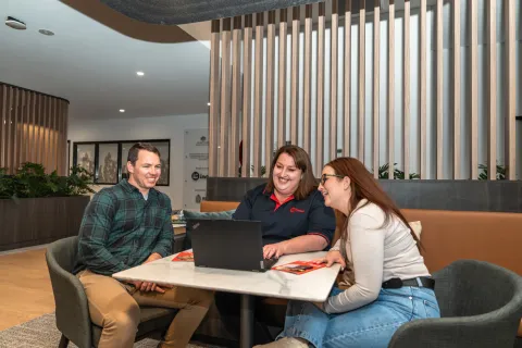 Three people seated at a table inside the Queanbeyan Veteran and Family Hub, looking at a laptop together.