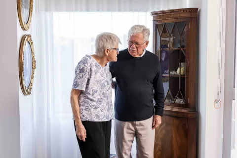 Two elderley people standing close together having a conversation.