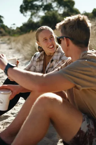 Two people sitting together in conversation on a sandy beach.