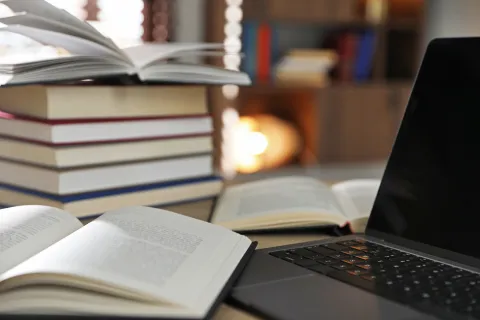 Open books stacked beside a laptop on a desk, with pages spread in a study setting.