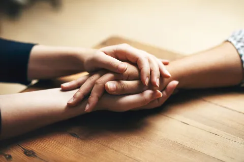 Close-up of two people holding hands across a table.