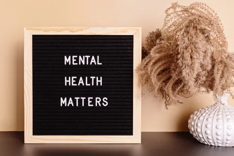 Sign reading “Mental Health Matters” beside a small vase of dried plants on a table.