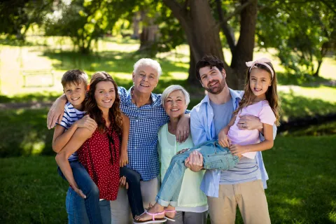 Multi‑generational family standing together in a park, with adults and children gathered close and facing the camera.