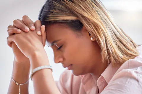 Close‑up of a person with hands clasped together near their face and head lowered.