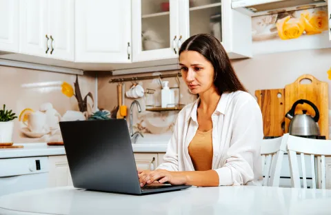A person sitting at a table in a kitchen using a laptop.