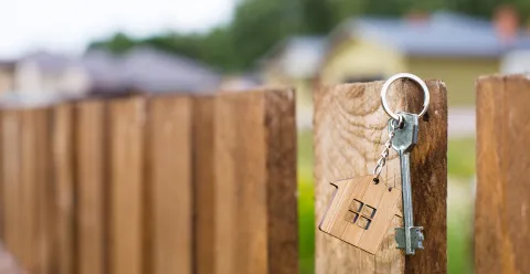 A key with a house-shaped keyring hanging on a wooden fence post.