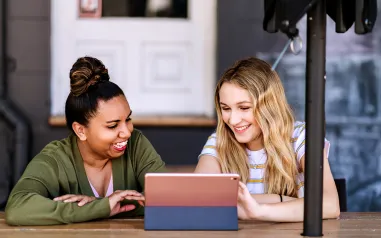 Two ladies smiling, while looking at an iPad screen.