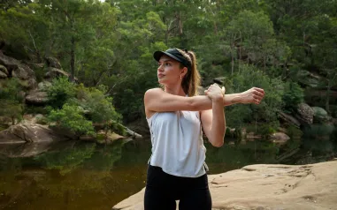 A woman stretching her arm by a creek. 