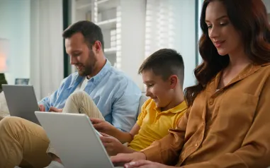A photo of a family sitting on a couch looking at their laptops.