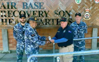 A man shaking hands with an Australian Defence Force member in front of a sign that says 'Air Base Recovery Squadron.'