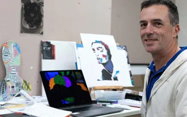 A man smiling sitting in front of artwork.
