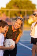 A child holding a ball on a netball court, near umpire and with other children nearby.
