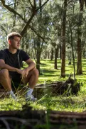 A person sitting on a fallen log in a forest area.