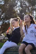 Two young children sitting outdoors in a park, blowing bubbles.
