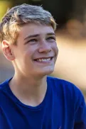 Close-up of teenage boy sitting outdoors, looking up at someone standing nearby.
