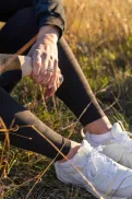 Close-up of a person clasping their hands while sitting in tall grass on a hillside.
