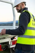 A person wearing a hard hat and high-visibility vest standing at the back of a work vehicle, holding the tray.