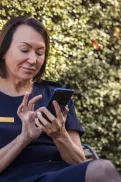 A person in Australian Defence Force uniform sitting on a bench in a garden setting, using a mobile phone.