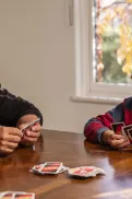 An adult and child sitting at a table playing a card game together.