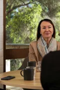 Three adults sitting around a table having a conversation over coffee in a casual indoor setting.