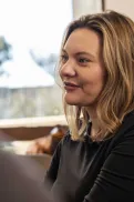 A person sitting indoors, facing and listening to someone in conversation.