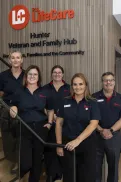 Five staff members in uniform standing together near a staircase inside the Hunter Veteran and Family Hub, with signage on the wall behind them.
