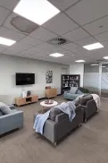 Seating area inside the Northern Adelaide Veteran and Family Hub with couches, a small table, television and shelves in a light-filled room.