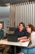 Three people seated at a table inside the Queanbeyan Veteran and Family Hub, looking at a laptop together.