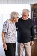 Two elderley people standing close together having a conversation.