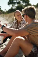 Two people sitting together in conversation on a sandy beach.
